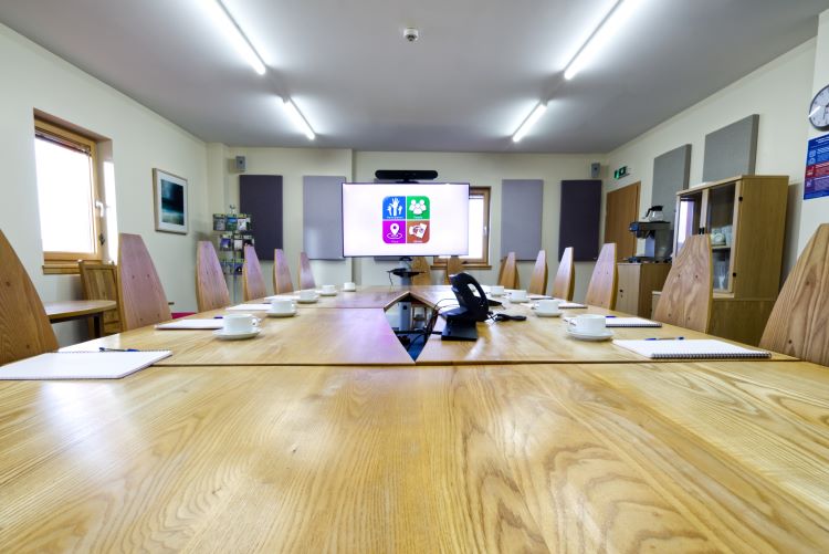 The Solarhus Boardroom, with a long meeting table with mugs and notebooks in front of each chair around the table. The big screen has the partnership logo on it.