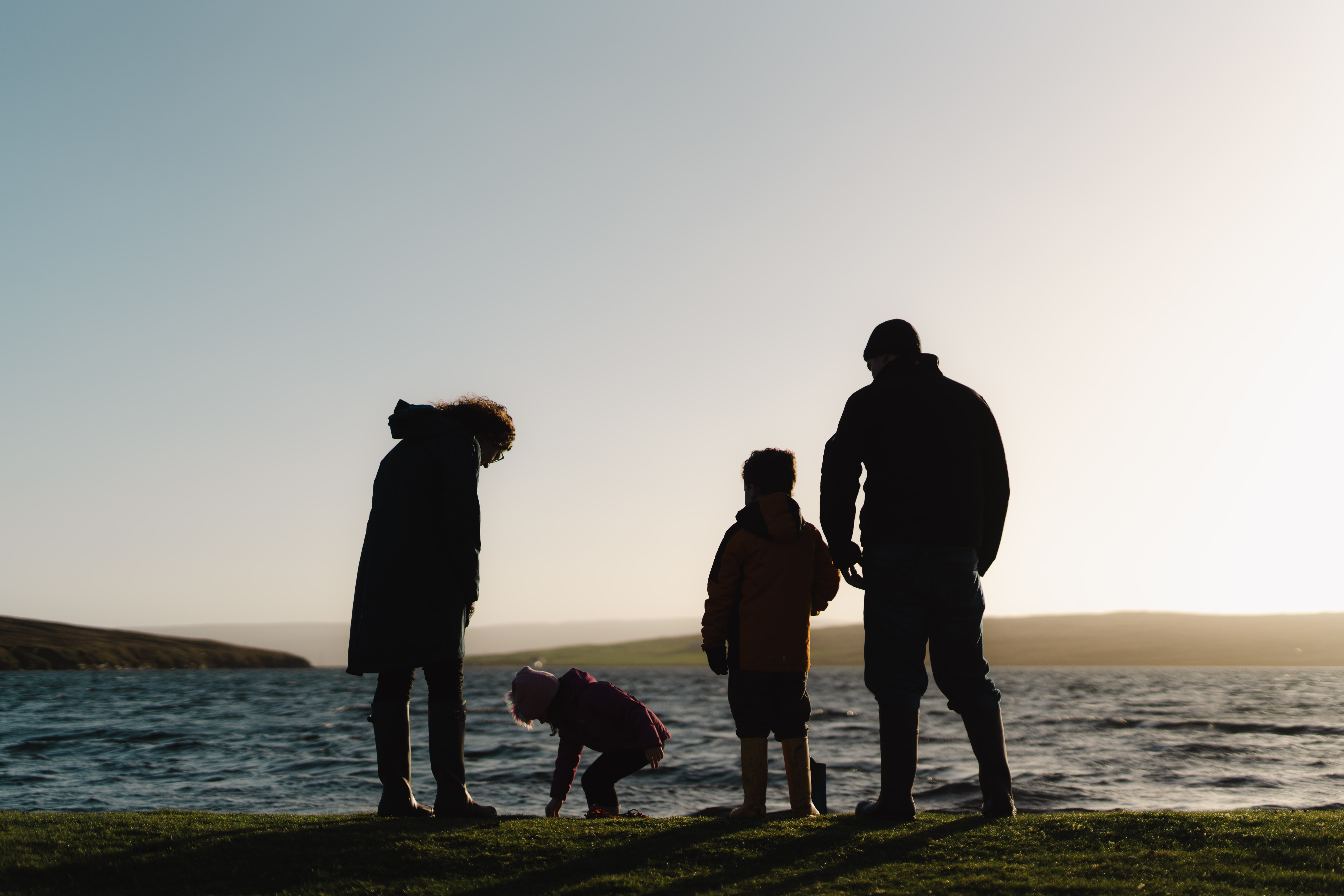 A family of four at the beach, silhouetted against the sun.
