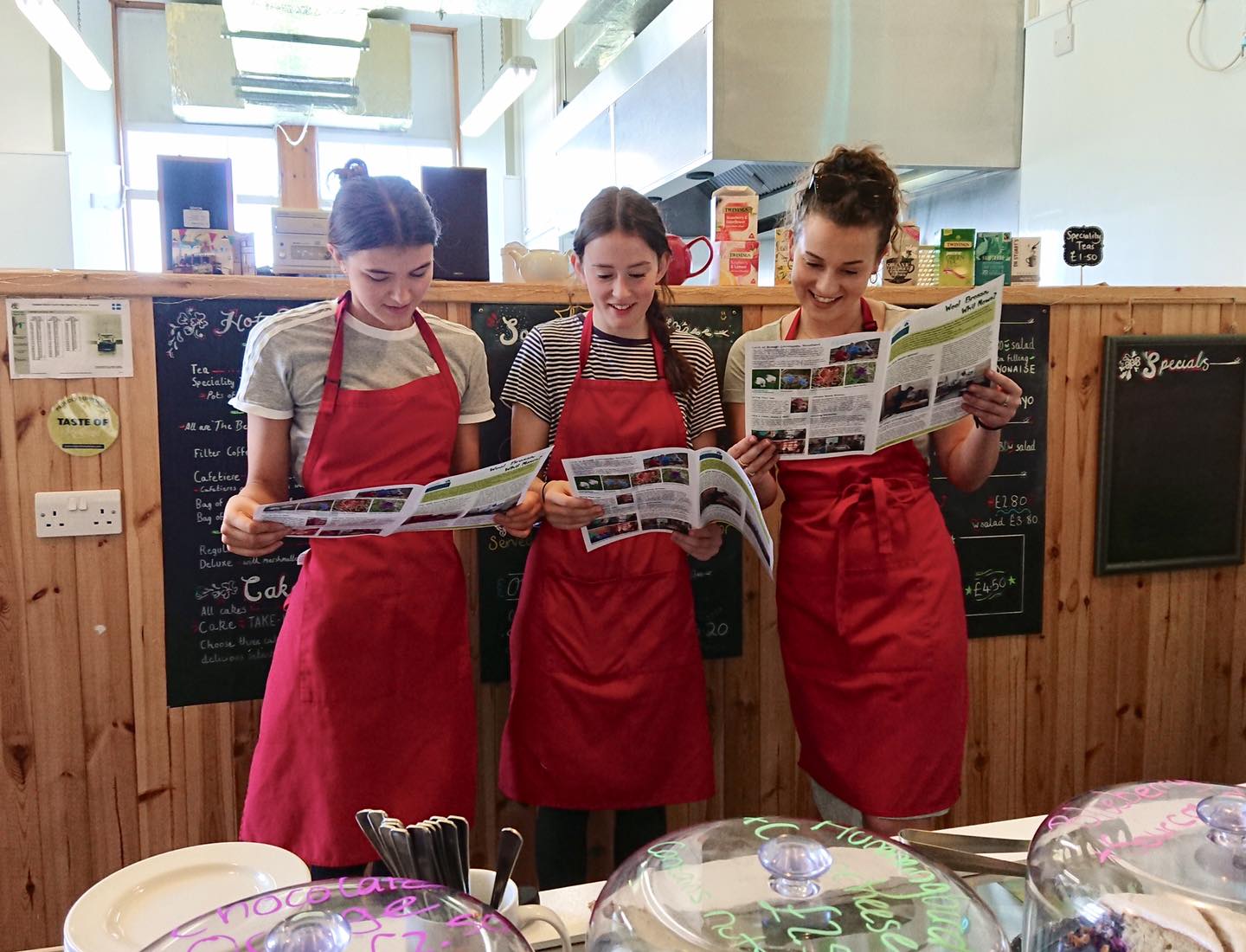 three members of staff at the Speldiburn cafe wearing red aprons, reading the Bressay newsletter
