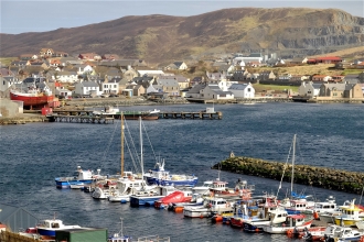 A photo of the Scalloway waterfront, with boats in the harbour and the hills in the background.
