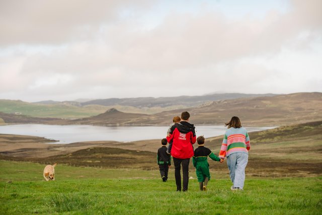 A family walking with a dog in a Shetland landscape, with hills, and the sea in the distance.