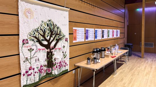 The Voices for Tapestry next to a table of drinks with the Seven Children posters pinned up behind.