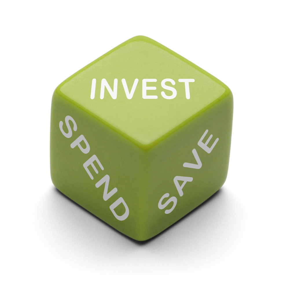 A green dice with 'Invest', 'Spend' and 'Save' written in white on three sides of the dice